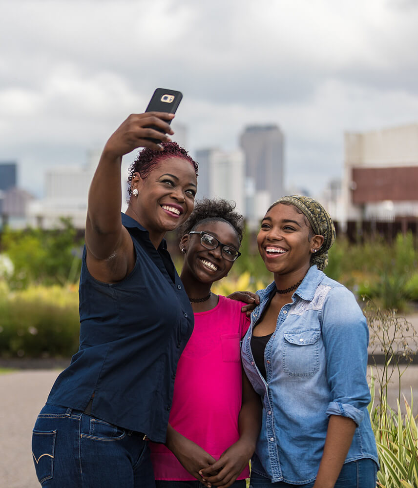 Three young women pose for a selfie with the New Orleans skyline in the background