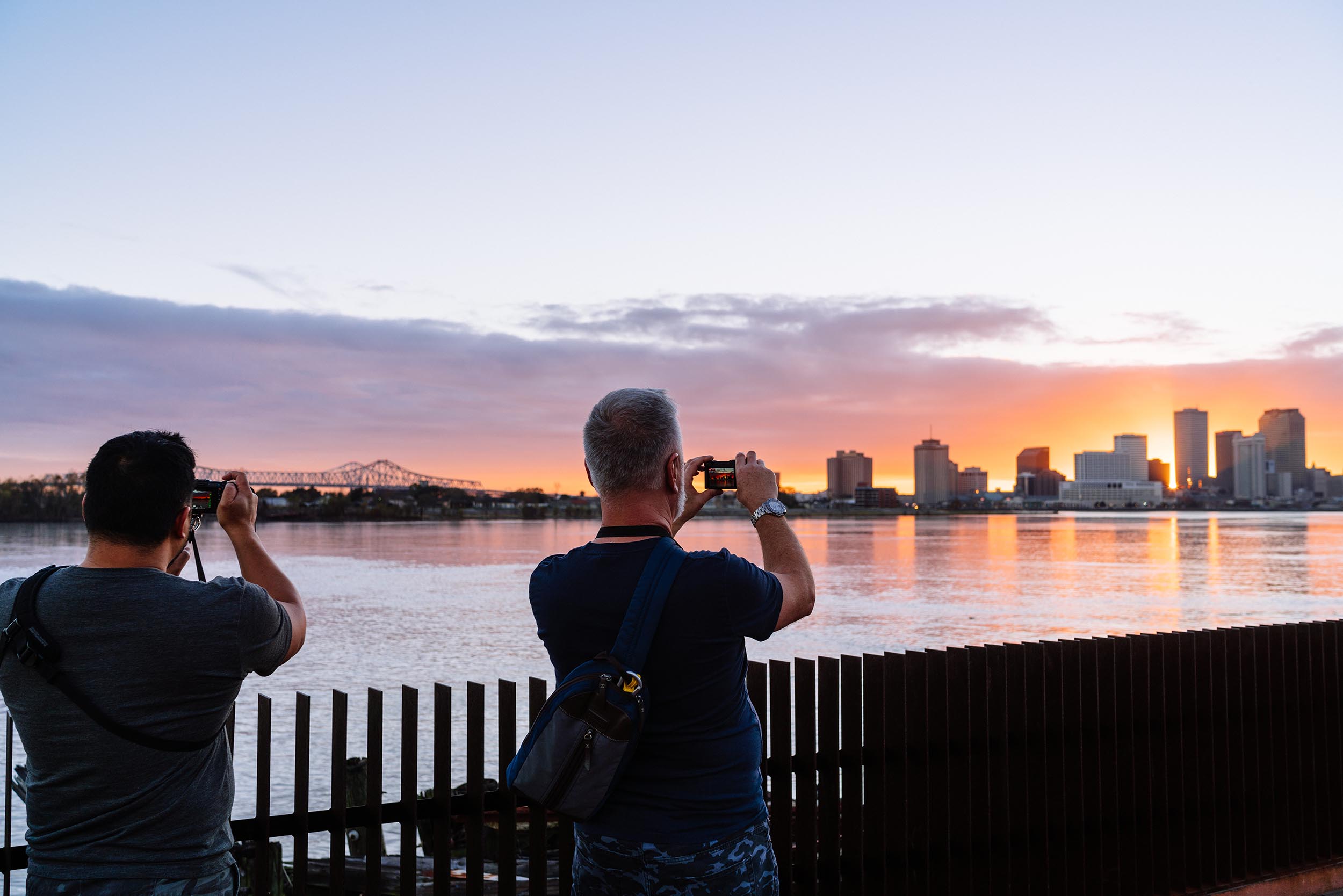 Two men in Crescent Park take photos of the New Orleans skyline across the water as the sun sets.